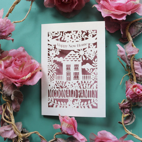 A laser cut card for first time buyers, with a house surrounded by flowers. Card says "Happy new home" and is personalised with the recipient/s' name in a line of text - A6 / Dusky Pink