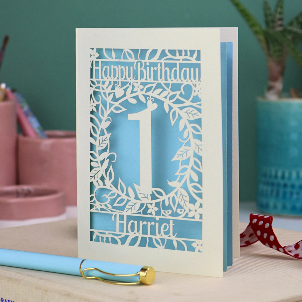 Laser cut 1st Birthday card with cut-out floral design on a desk with stationery items