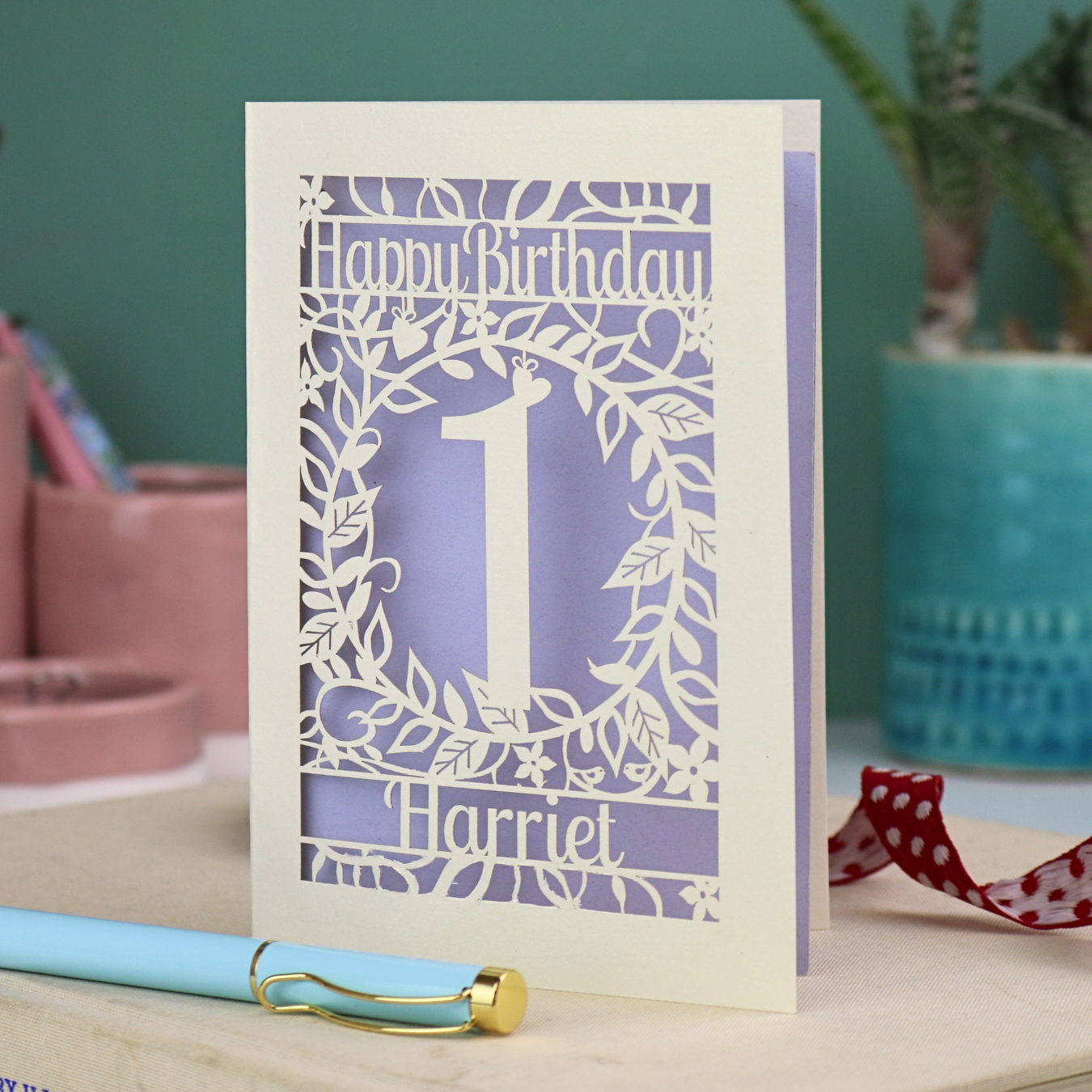 Laser cut 1st Birthday card with cut-out floral design on a desk with stationery items