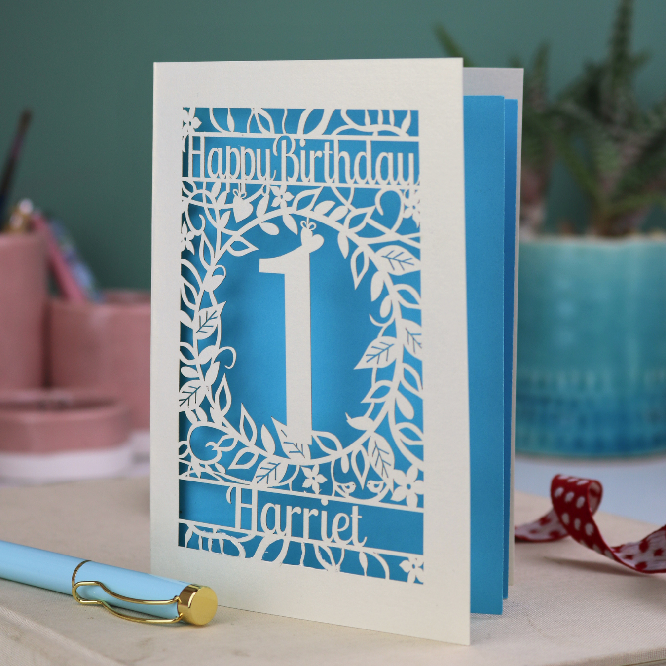 Laser cut First Birthday card with cut-out floral design on a desk with stationery items
