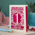 Laser cut 1st Birthday card with cut-out floral design on a desk with stationery items