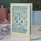 A laser cut floral birthday card, personalised with the age 38 and the name Carrie, with floral border in cream and a coloured paper insert. 