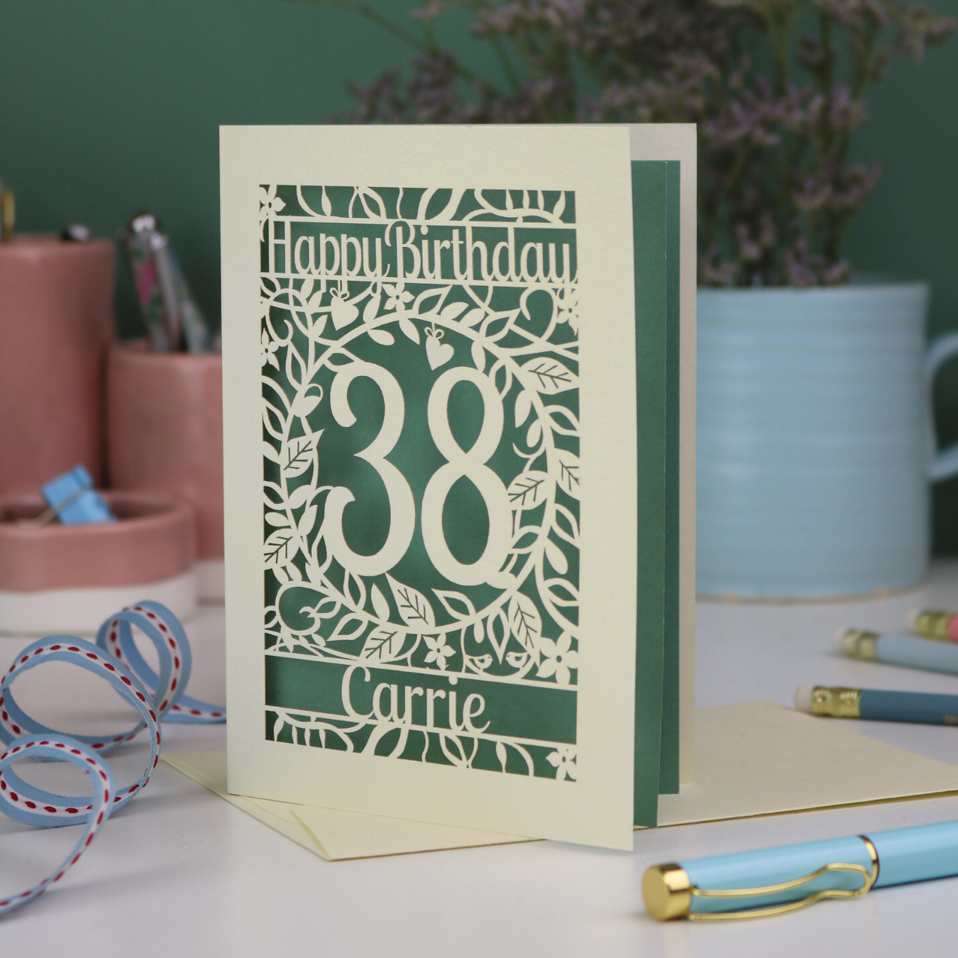 A cut out floral birthday card, personalised with the age 38 and the name Carrie, with floral border in cream and a coloured paper insert. 