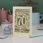 A personalised 70th birthday card, with floral cut out design and 'Happy Birthday', with a name at the bottom and a big number 70 in the centre. 