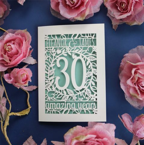 A laser cut anniversary card. Card is laser cut with a  line of text at the top that says "Eleanor & James". There is a number 30 inside a leafy border and a line of text at the bottom that says "amazing years".