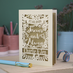 Personalized wedding card with red and cream cut out "forever and always" and floral design, personalised with a date and first names of the couple, on a desk with stationery items.