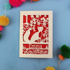 Decorative first birthday card with cut-out design of a fox and floral patterns on a blue background with colourful pom-poms.