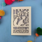 Personalised first birthday card with cut-out design of a fox and floral patterns on a blue background with colourful pom-poms.