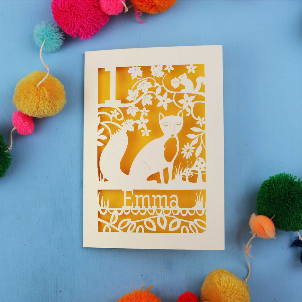 Keepsake Personalised first birthday card with cut-out design of a fox and floral patterns on a blue background with colourful pom-poms.