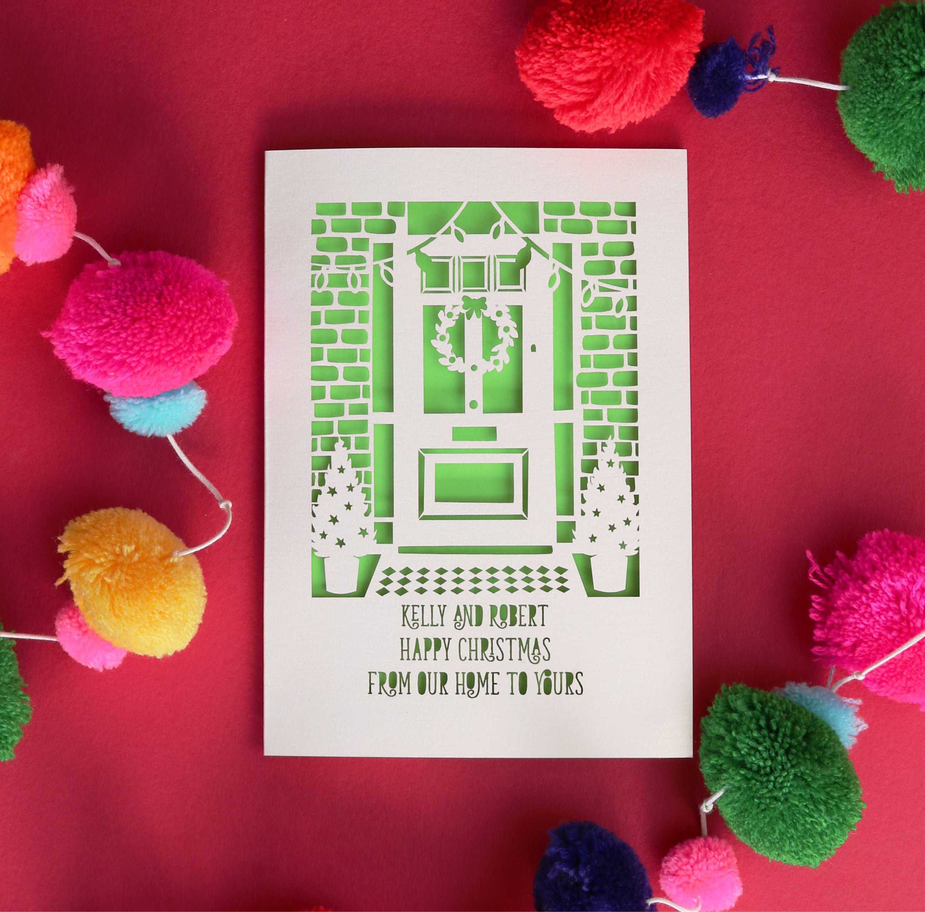 A personalised Christmas card, laser cut with the words "Happy Christmas, from our home to yours" and a laser cut image of a door with a wreath and two small Christmas trees either side of the door. Shop other online greetings card designs in our online card shop.