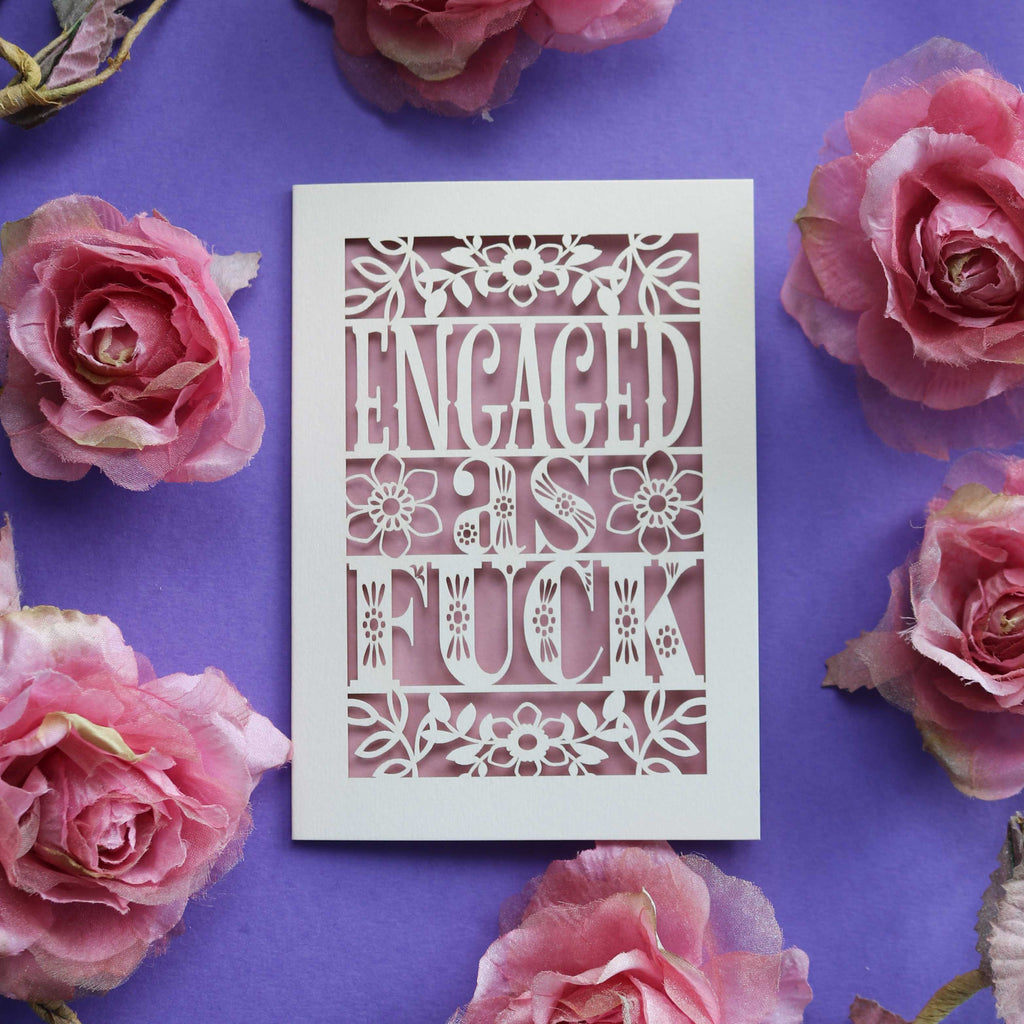 A cream and dusky pink engagement card with "Engaged as Fuck" in cut out text