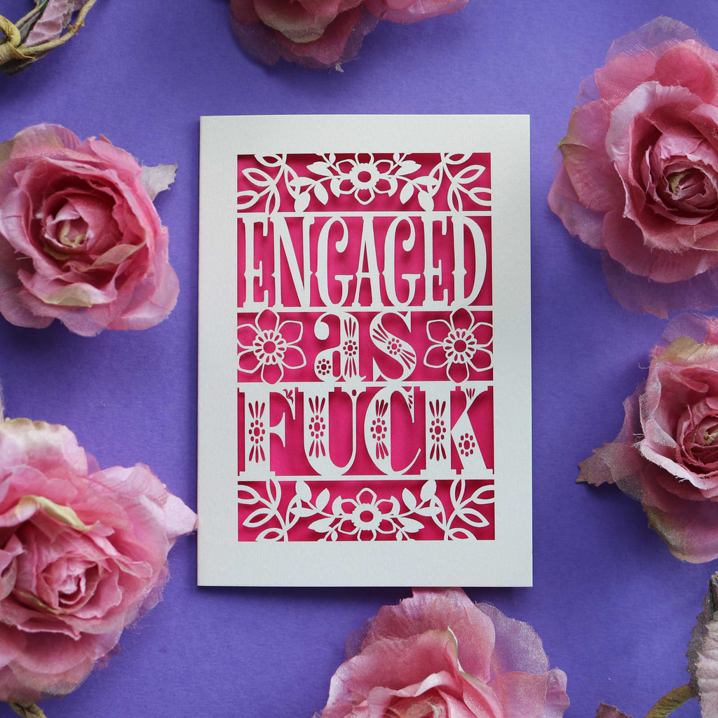 A funny engagement card for friends. Engaged as Fuck is cut out of a cream card with a shocking pink background