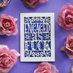 A funny engagement card for friends. Engaged as Fuck is cut out of a cream card with a violet background