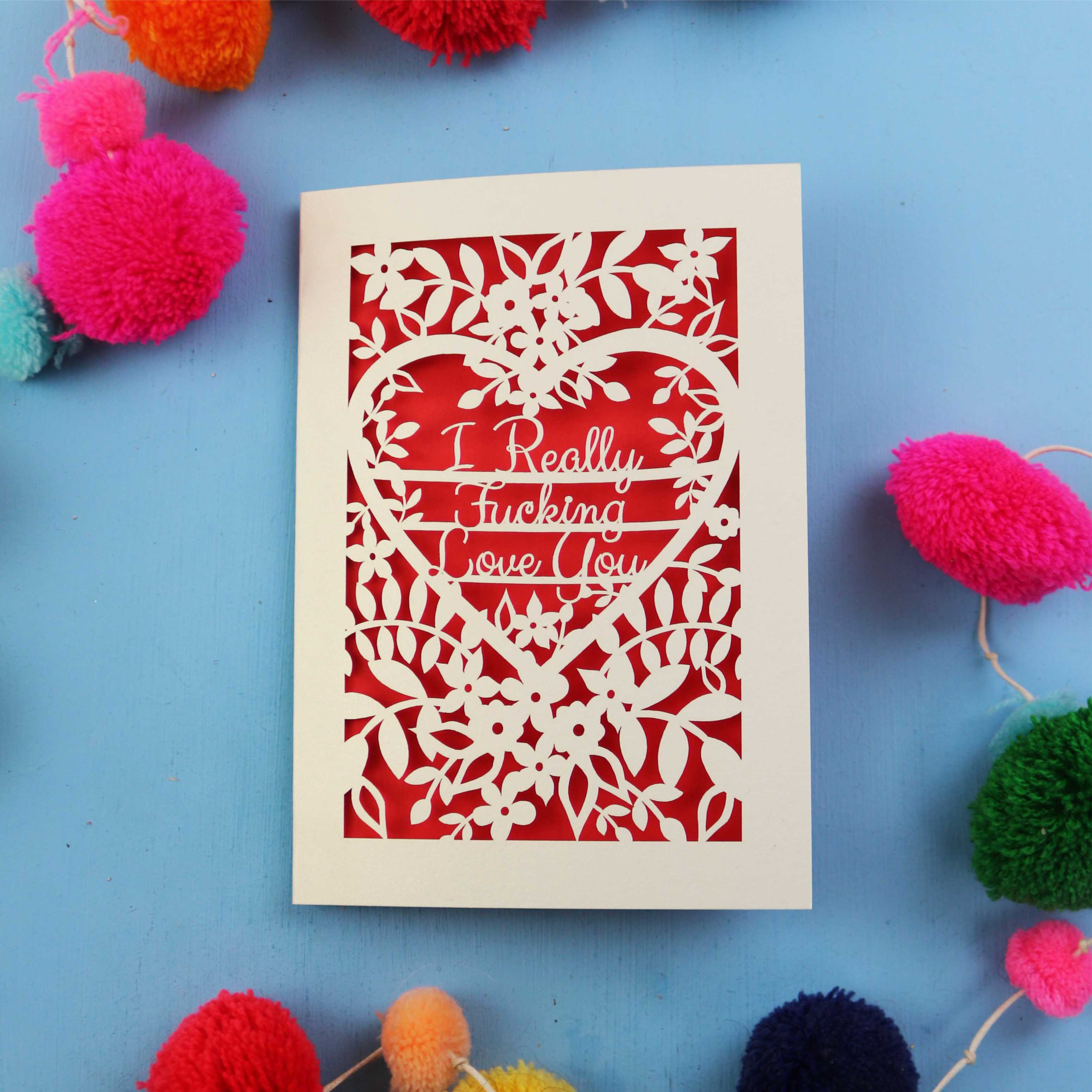 laser cut funny Valentine's Card with floral design and text on a blue background with colourful pom-poms