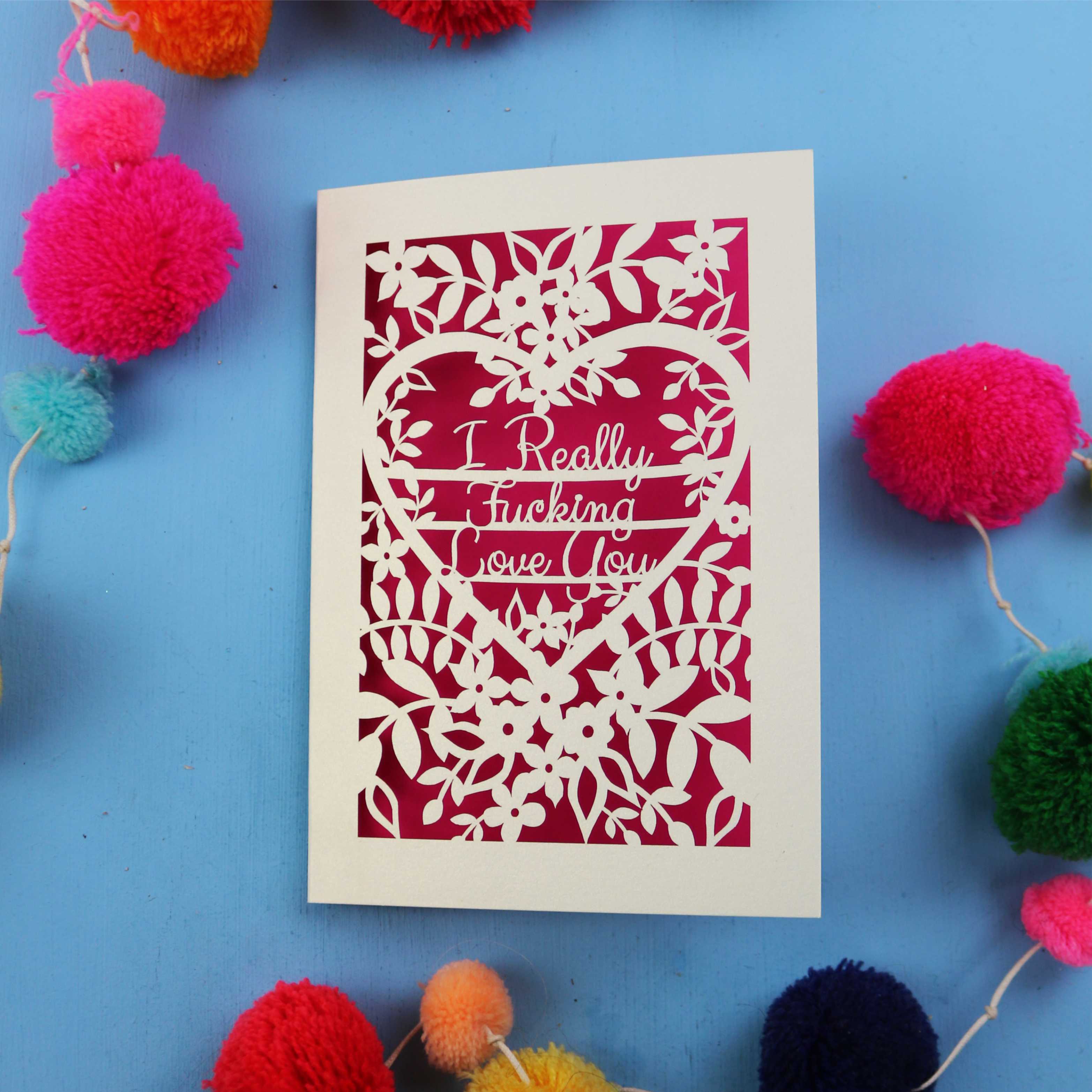 Sweary Valentine's Card with floral design and text on a blue background with colourful pom-poms