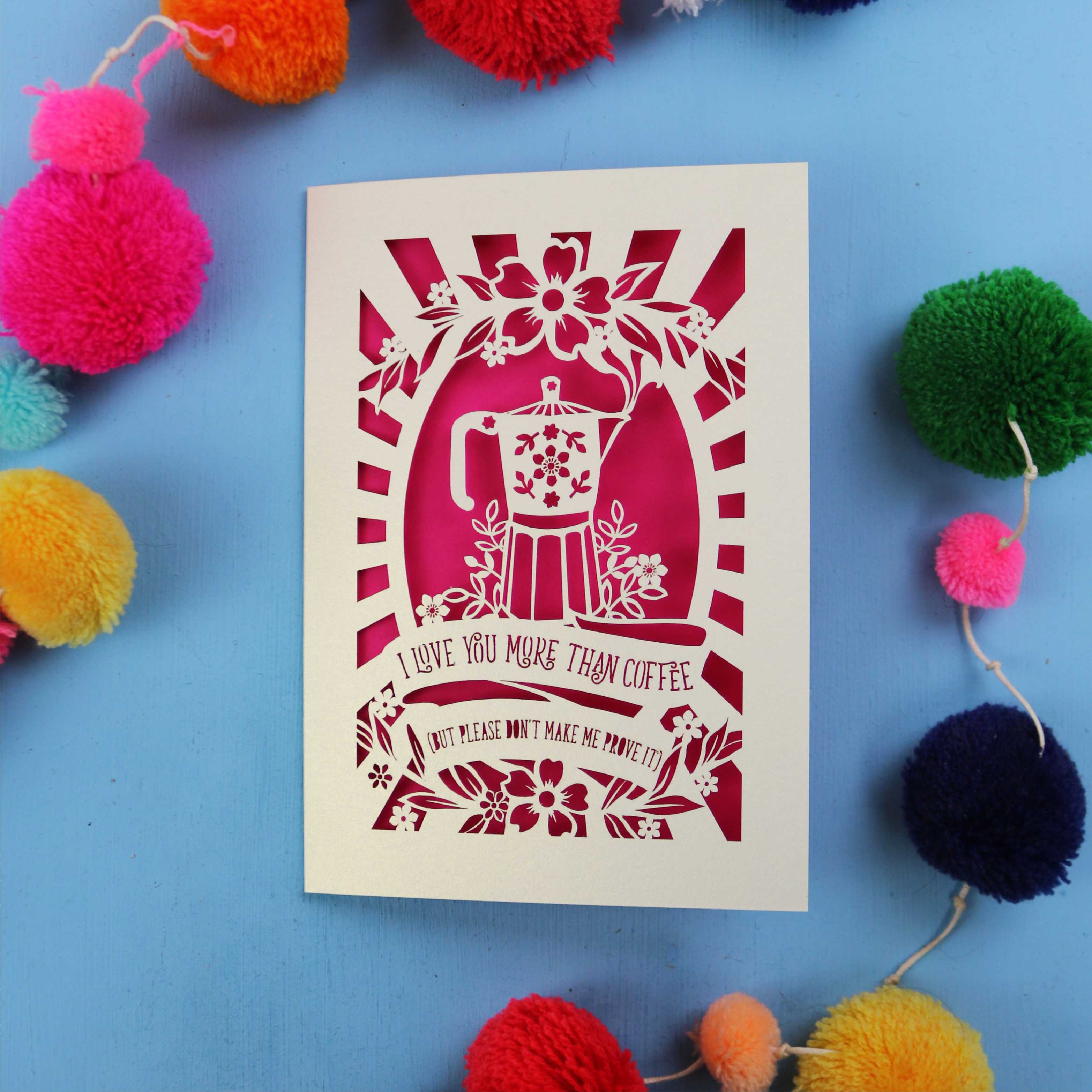 Funny Laser cut Valentine's card with coffee-themed design and the words "I love you more than coffee, but please don't make me prove it)" on a blue background with colourful pom-poms.