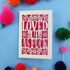 Laser cut funny Valentine's Card with 'LOVED UP AS FUCK' design on a blue background with colourful pom-poms.