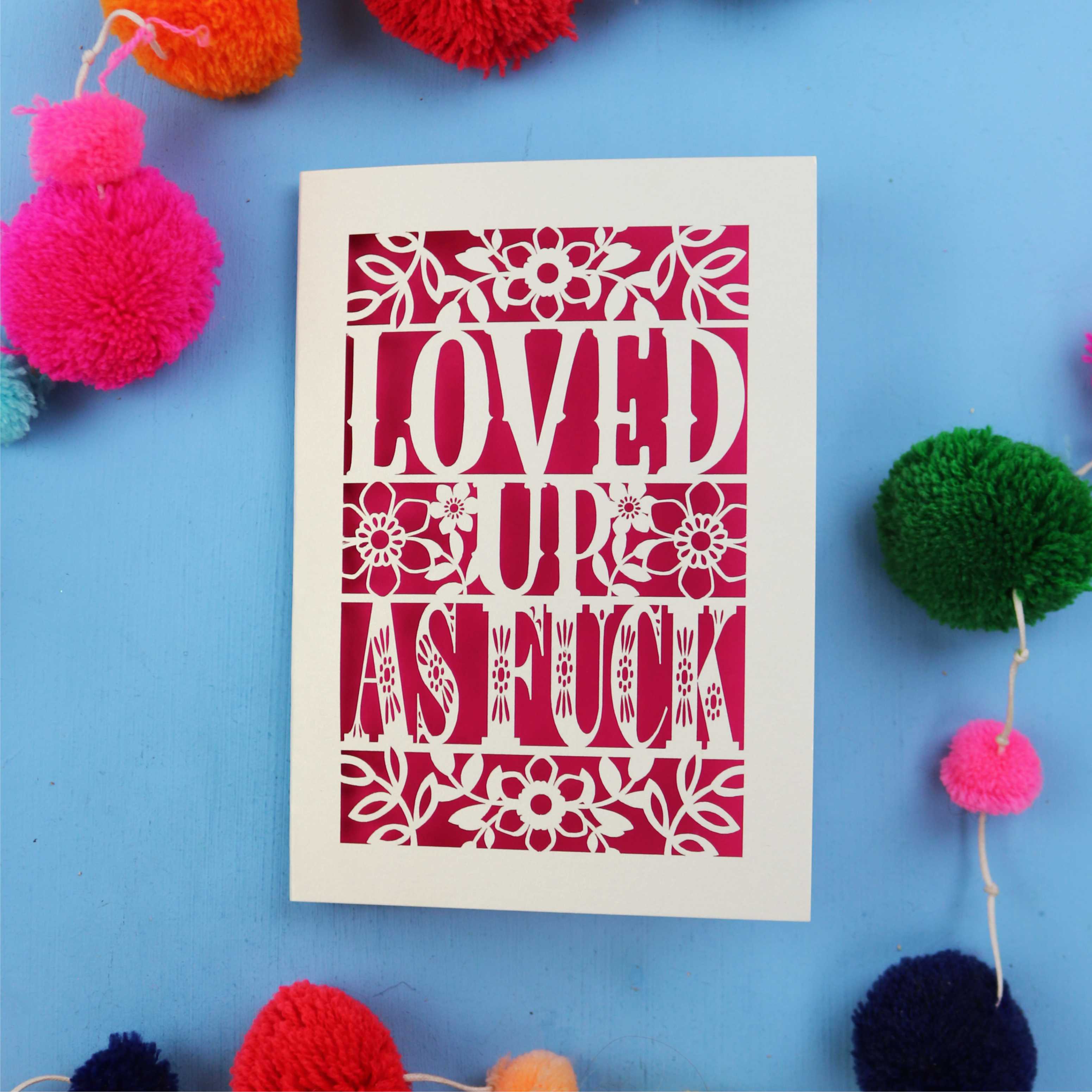 Laser cut funny Valentine's Card with 'LOVED UP AS FUCK' design on a blue background with colourful pom-poms.