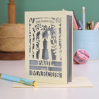 Personalized card with laser-cut design of two men holding hands, on a desk with stationery items.