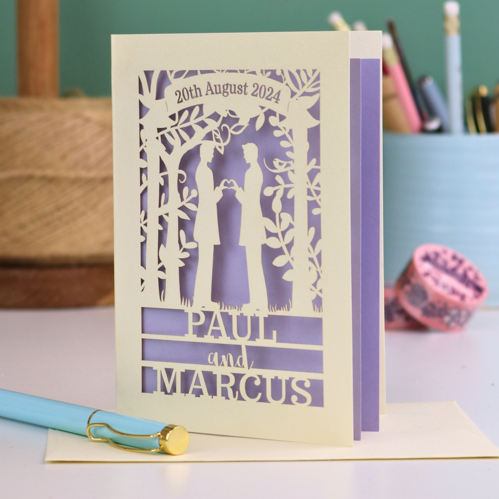 Personalized gey wedding card with laser-cut design and text '20th August 2024, Paul and Marcus' on a desk.