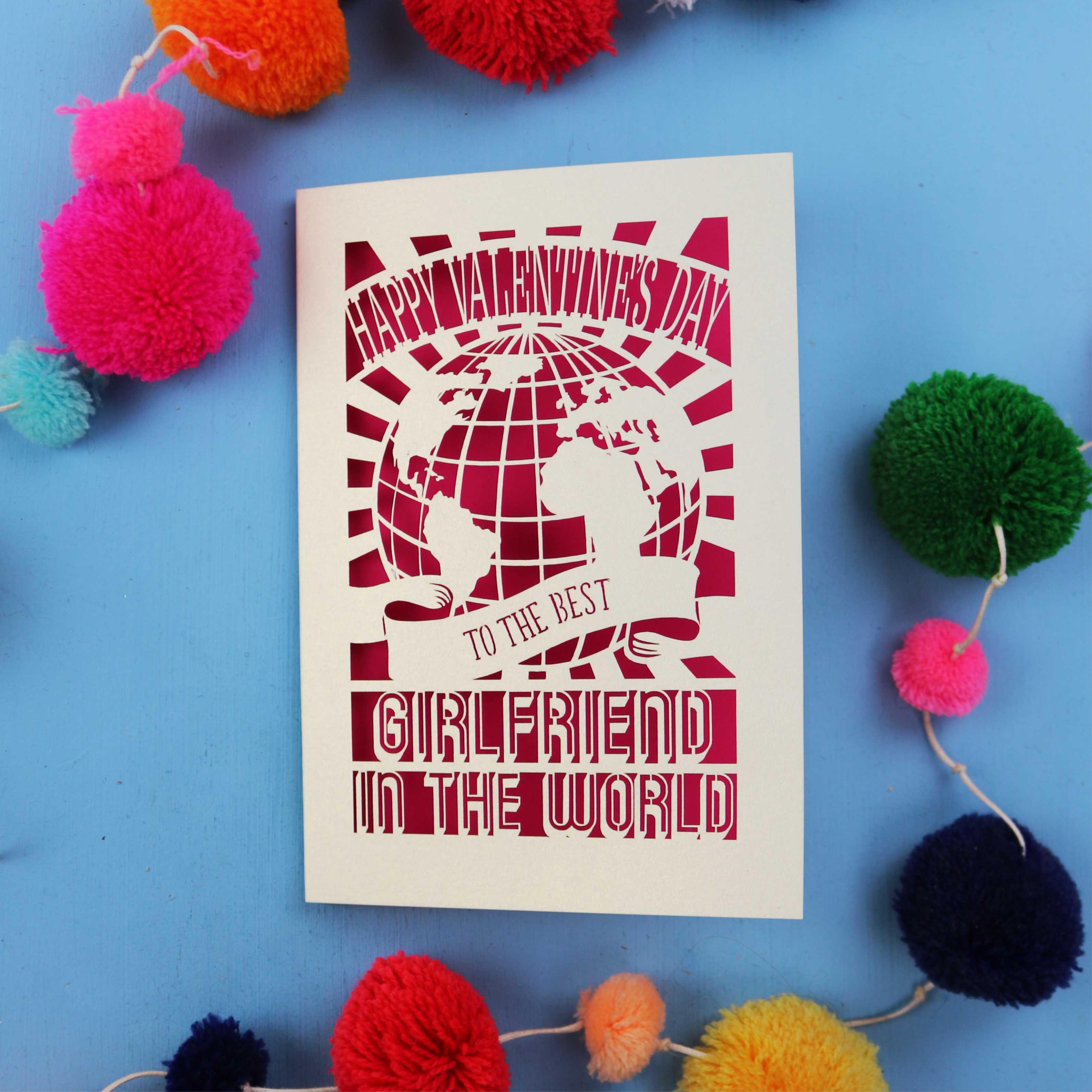 A laser cut girlfriend Valentine's card that features a paper cut out World design and the words "Happy Valentine's Day to the Best Girlfriend in the World"