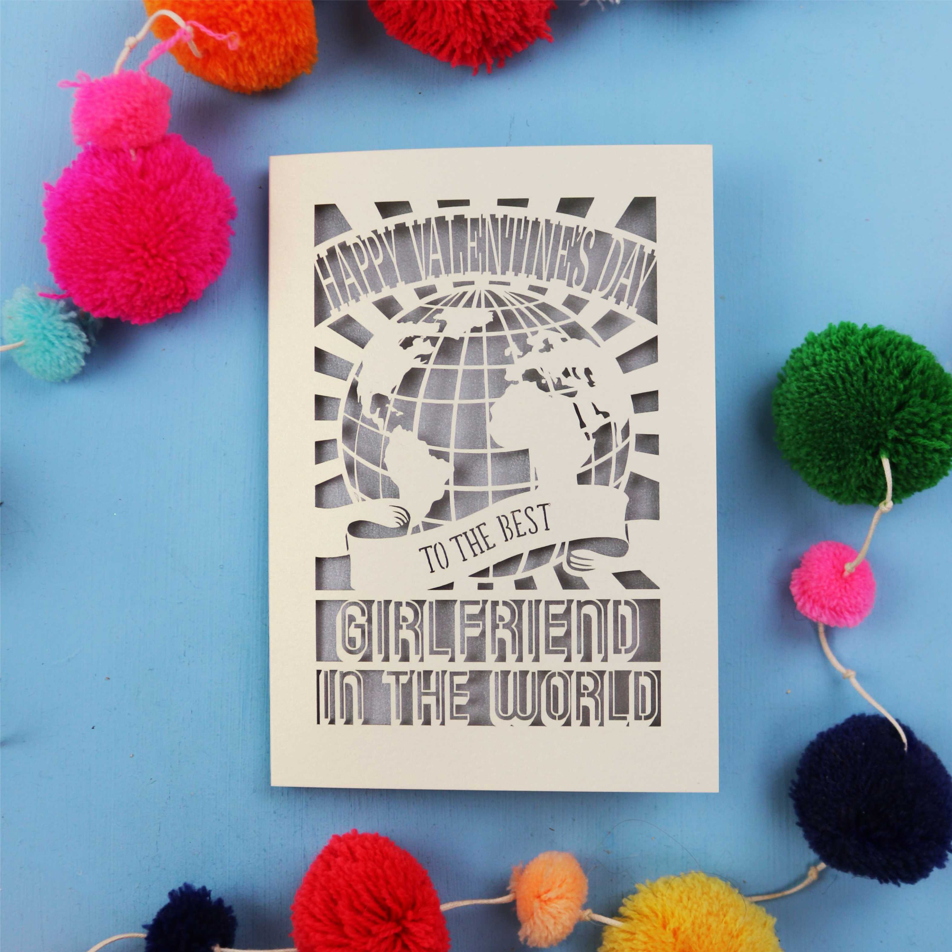 A laser cut girlfriend Valentine's card that features a paper cut out World design and the words "Happy Valentine's Day to the Best Girlfriend in the World"