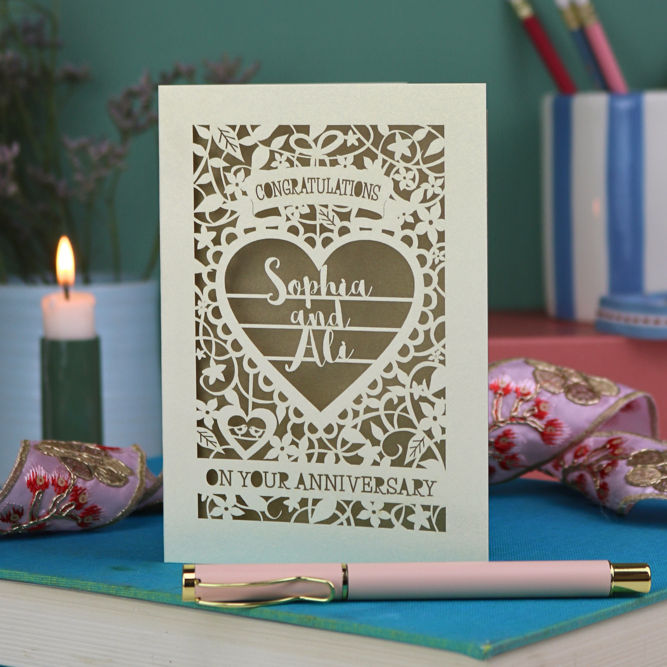Personalised anniversary card with decorative heart design on a table with candles and flowers.