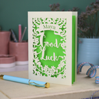 Laser-cut 'Good Luck' card with decorative elements and personalised with the name "Maya" in stencil font on a banner above the text 'Good Luck' in a script font.