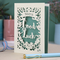 Laser-cut 'Good Luck' card with decorative elements and personalised with the name "Maya" in stencil font on a banner above the text 'Good Luck' in a script font.