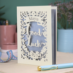 Laser-cut 'Good Luck' card with decorative elements and personalised with the name "Maya" in stencil font on a banner above the text 'Good Luck' in a script font.