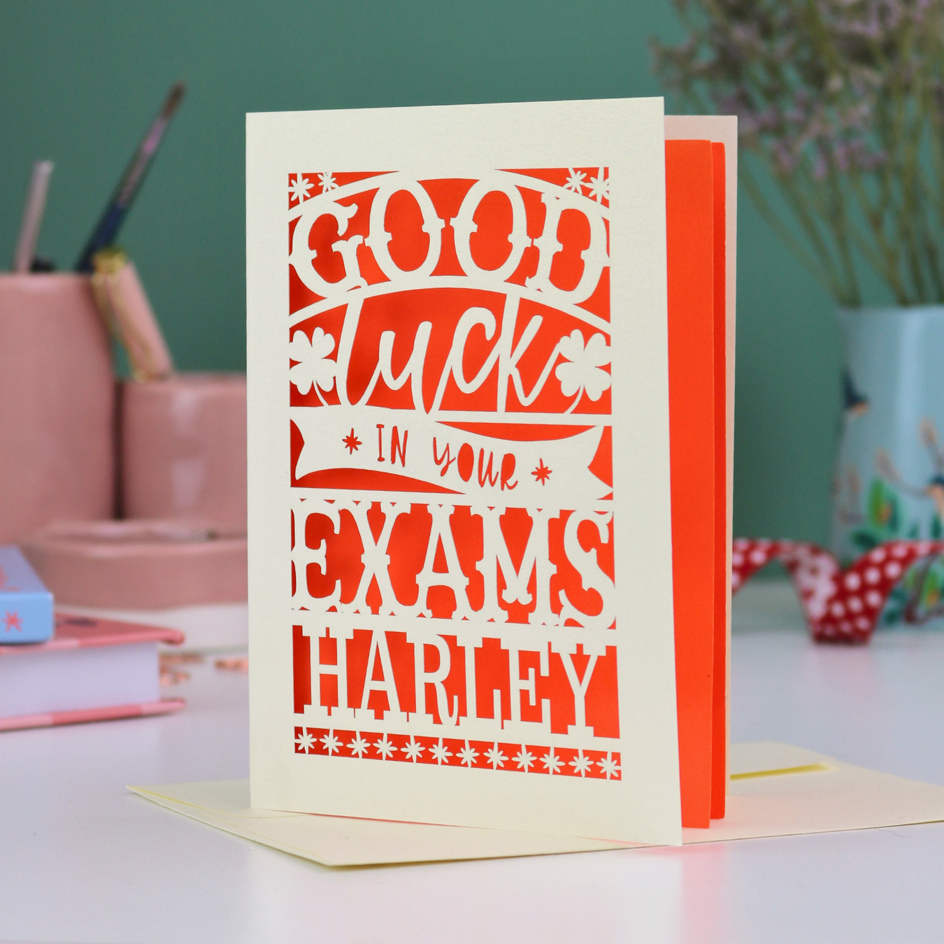 Greeting card with 'Good luck in your exams Harley' text on a desk with stationery items.