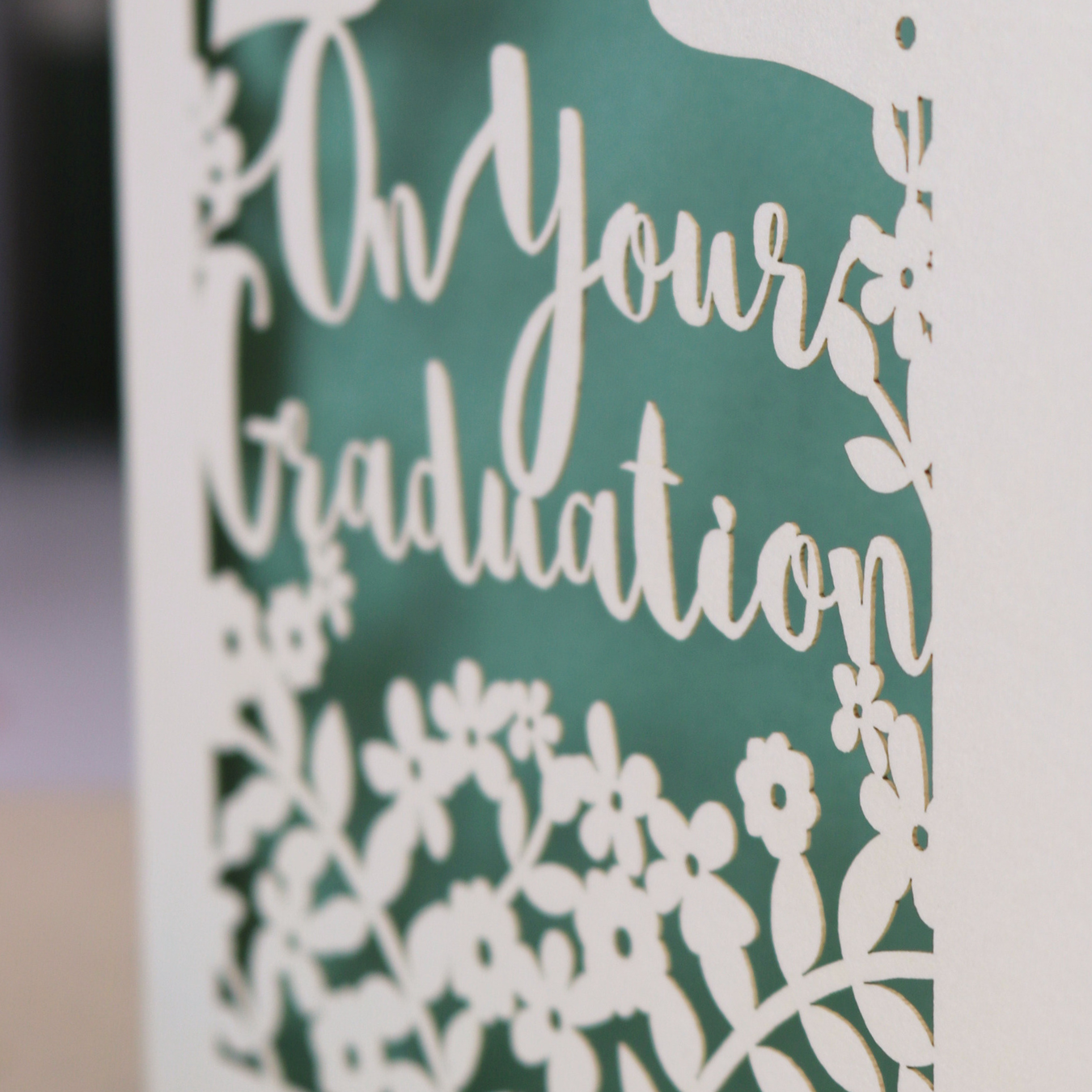 Laser cut Graduation card with personalized name 'Abbie' and floral cut out design, on a table with decorative elements.