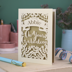 Laser cut Graduation card with personalized name 'Abbie' and floral cut out design, on a table with decorative elements.