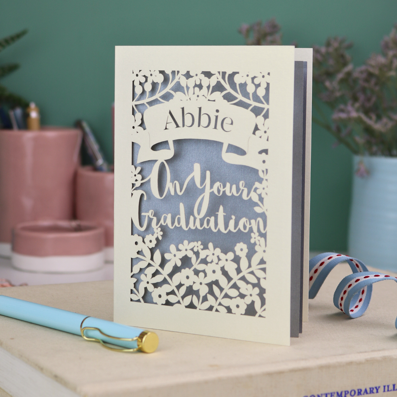 Paper cut Graduation card with personalized name on a desk with decorative items