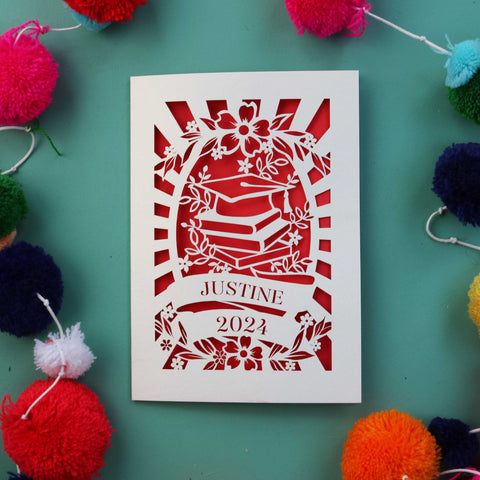 A personalised graduation card with a cap on some books and a name and year in a banner - A6 (small) / Bright Red