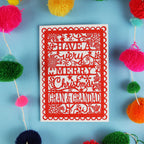 Red Christmas card with personalized message surrounded by colourful pom-poms on a blue background