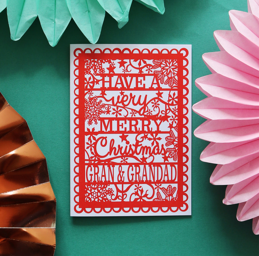 A red A6 Christmas card with  'Have a very merry Christmas Gran & Grandad' text, placed on a green background
