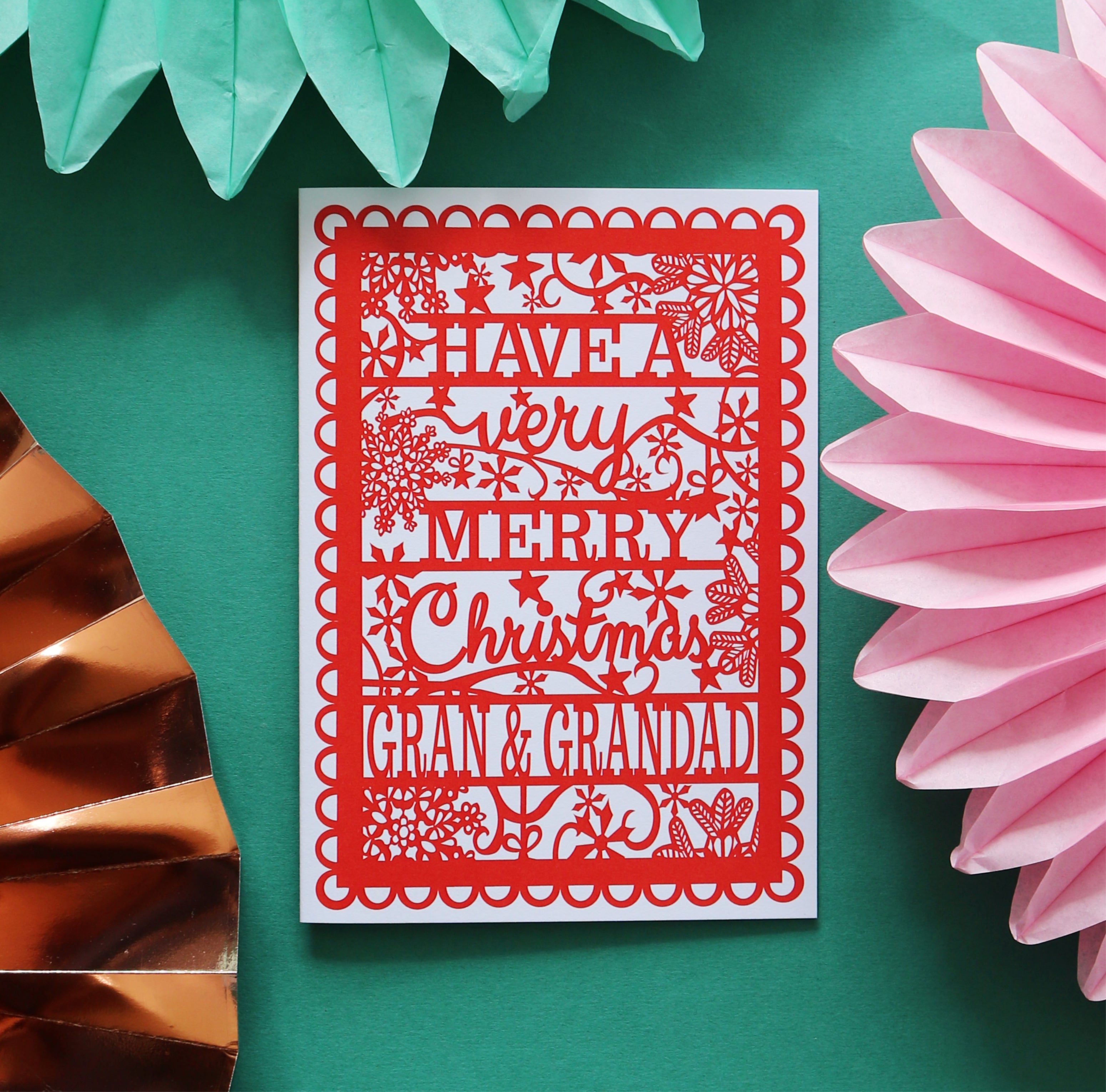 A red A6 Christmas card with  'Have a very merry Christmas Gran & Grandad' text, placed on a green background