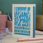 A laser cut wedding card with cut out text, 'Happily Ever After' in a script font, personalised with 'Anna & John, 14.06.2026'