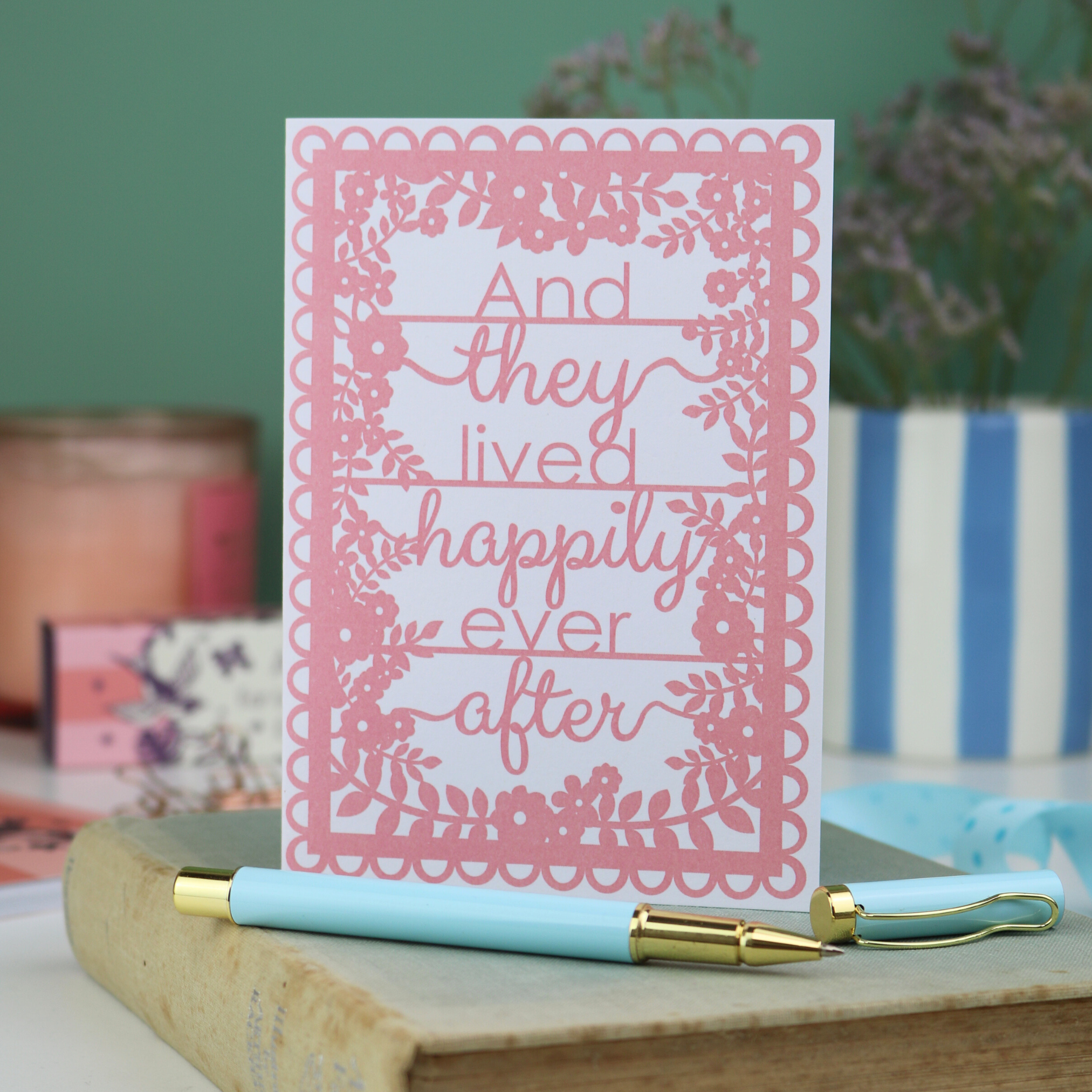 Pink wedding card with 'And they lived happily ever after' text on a wooden surface with a pen.