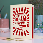 Red and cream laser cut Bar Mitzvah card with 'Happy Bar Mitzvah Jack' text on a desk with stationery items.