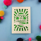 Cut out card with 'Happy Bar Mitzvah Noah' text on a blue background with colourful pom-poms.