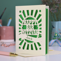 Green and cream laser cut Bar Mitzvah card with 'Happy Bar Mitzvah Jack' text on a desk with stationery items.