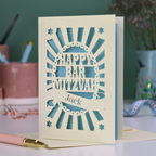 Blue and cream laser cut Bar Mitzvah card with 'Happy Bar Mitzvah Jack' text on a desk with stationery items.