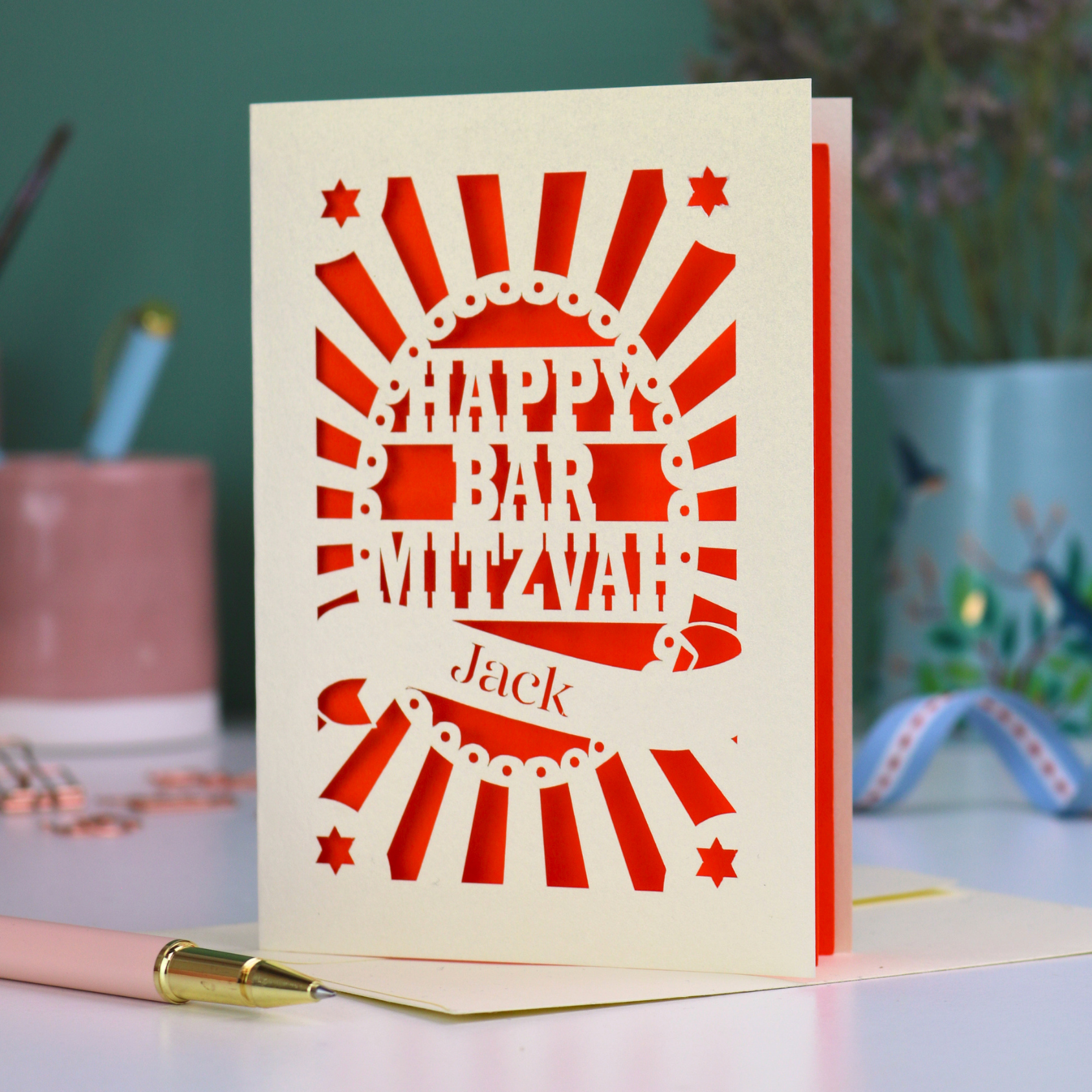 Orange and cream laser cut Bar Mitzvah card with 'Happy Bar Mitzvah Jack' text on a desk with stationery items.
