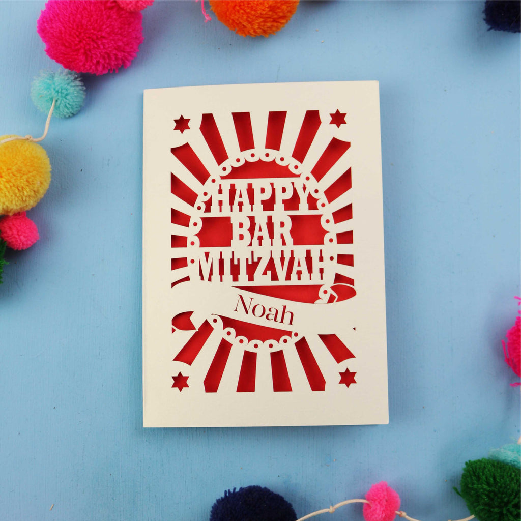 Laser Cut card with 'Happy Bar Mitzvah Noah' text on a blue background with colourful pom-poms.
