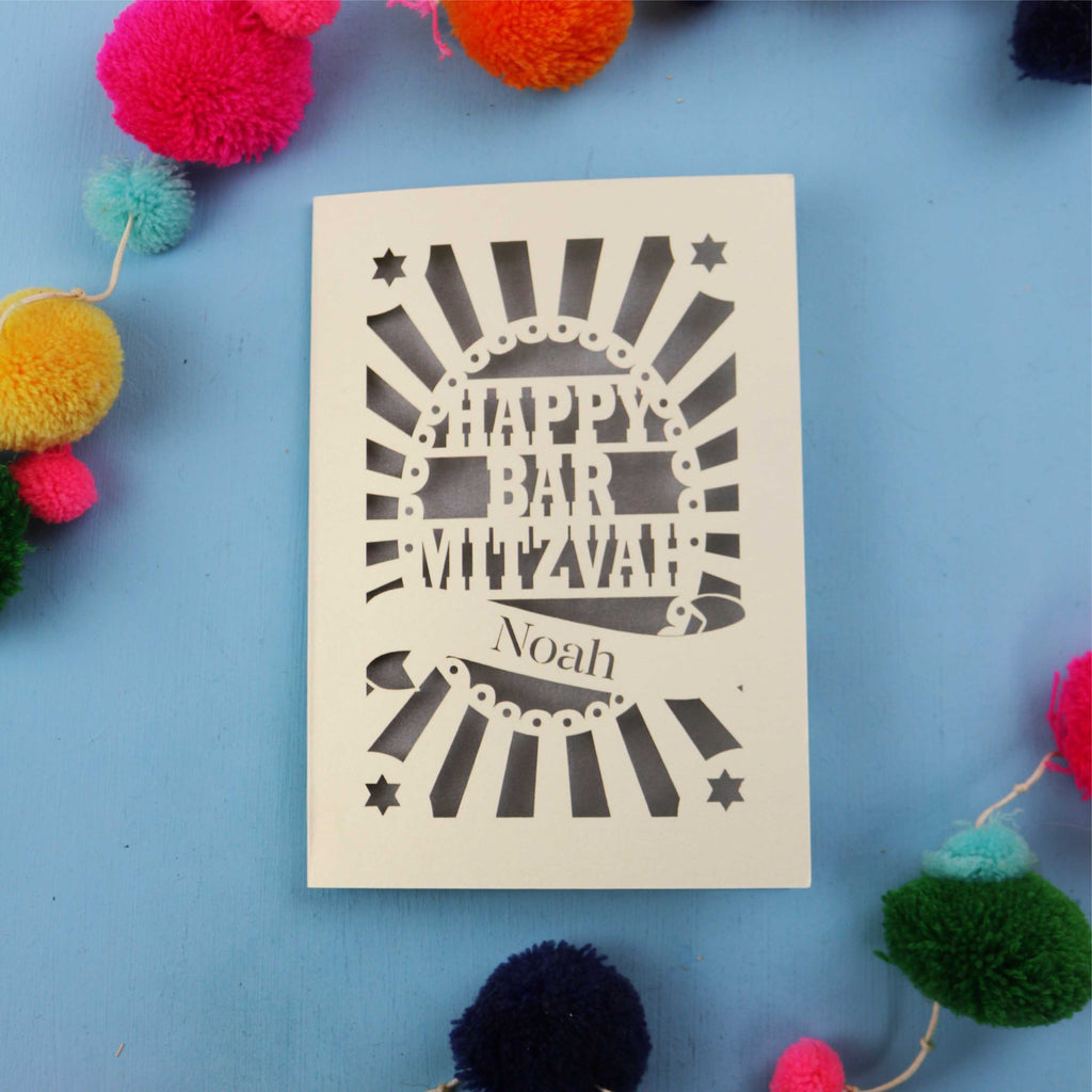 Personalised Bar Mitzvah card with 'Happy Bar Mitzvah Noah' text on a blue background with colourful pom-poms.