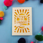 Laser Cut card with 'Happy Bar Mitzvah Noah' text on a blue background with colourful pom-poms.