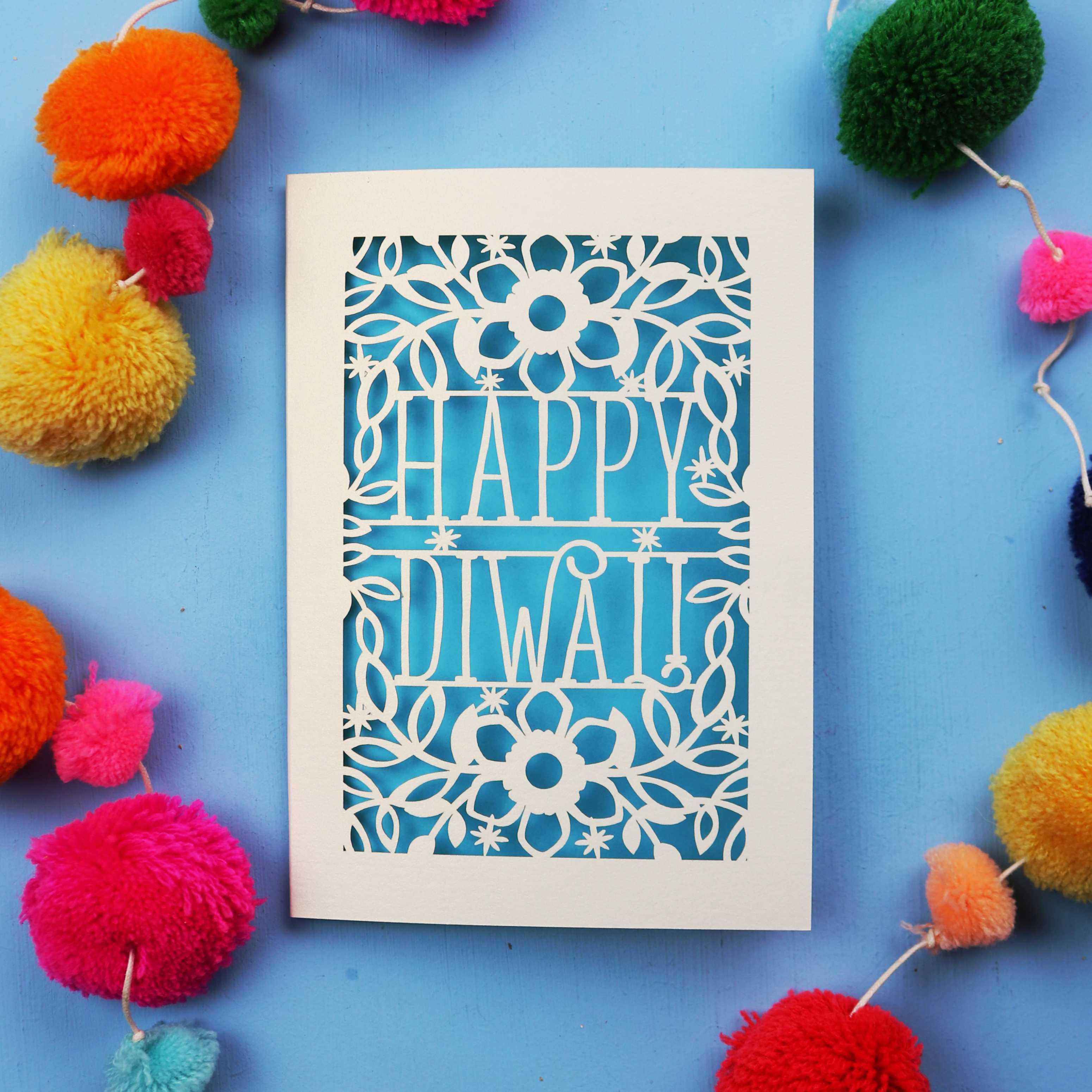 Laser Cut Diwali Card with 'Happy Diwali' design surrounded by colourful pom-poms on a blue background