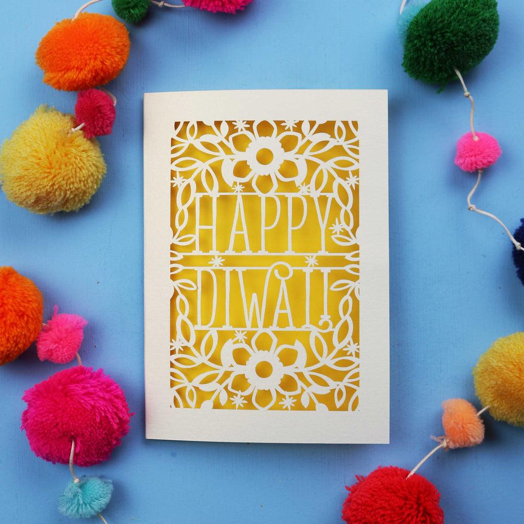 Laser Cut Diwali Card with 'Happy Diwali' design surrounded by colourful pom-poms on a blue background